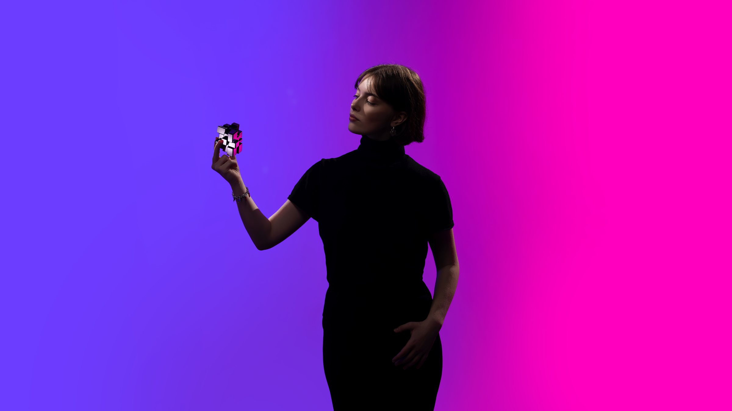 Sofiia Yanovska in silhouette, holding up a small puzzle cube against a violet and pink backdrop